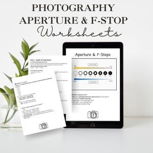 Könnte beinhalten: Ein schwarzes Tablet zeigt ein Fotografie-Arbeitsblatt mit dem Titel "Aperture & F-Stops". Gedruckte Arbeitsblätter mit Text über Blende und F-Zahl sind ebenfalls vorhanden. Das Bild enthält eine Glasvase mit grünen Blättern.