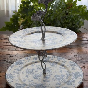 May include: Two-tiered serving stand with floral patterned plates. The plates are cream-colored with a blue floral design. The stand is silver-colored and features a ginkgo leaf design. Perfect for displaying desserts or appetizers.