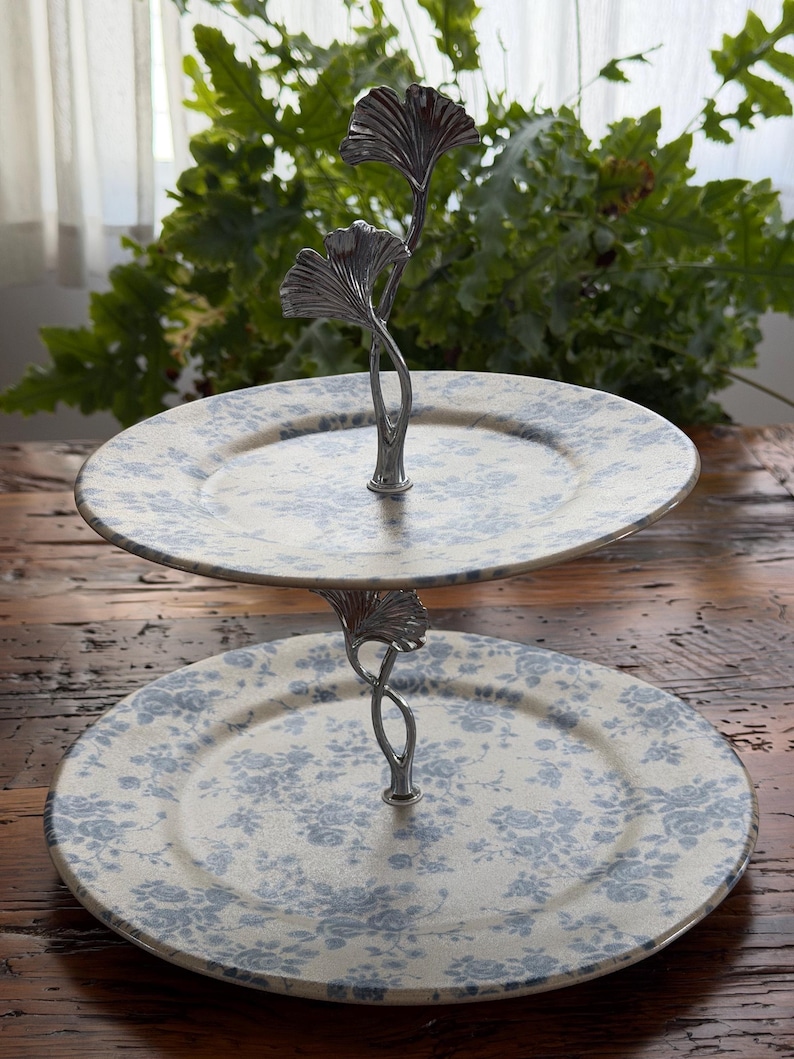 May include: Two-tiered serving stand with floral patterned plates. The plates are cream-colored with a blue floral design. The stand is silver-colored and features a ginkgo leaf design. Perfect for displaying desserts or appetizers.