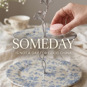 May include: A two-tiered serving stand with a floral design in blue and white. The stand has a silver metal handle with a leaf design. The text "SOMEDAY IS NOT A DAY FOR GOOD CHINA" is visible. The text "UPCYCLED & ONE-OF-A-KIND" and "HANDCRAFTED FOR THE EVERYDAY" are also visible.