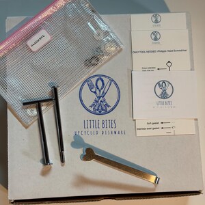 May include: A box containing upcycled dishware hardware. Includes a clear mesh bag labeled "HARDWARE", metal tools, and cards with instructions and the "LITTLE BITES UPCYCLED DISHWARE" logo. The box is white with blue text and graphics.