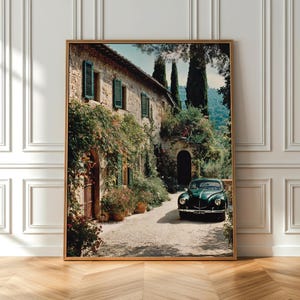 Könnte beinhalten: Ein gerahmter Kunstdruck, der ein Steingebäude mit grünen Fensterläden und Kletterpflanzen zeigt, mit einem dunkelgrünen Oldtimer auf einer Kiesauffahrt. Hohe Zypressen stehen im Hintergrund unter einem klaren blauen Himmel.