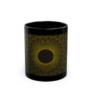 May include: Black ceramic mug with a gold geometric pattern. The design is a radial pattern with a central dark circle. The mug is cylindrical and has a glossy finish. The mug is suitable for hot or cold drinks.