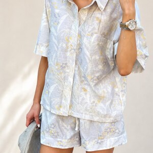 Puede incluir: Conjunto de camisa y pantal&oacute;n corto de lino azul claro con estampado floral amarillo y blanco. La camisa de manga corta tiene botones en la parte delantera y cuello. El pantal&oacute;n corto tiene cintura con cord&oacute;n. Tambi&eacute;n se ve un reloj plateado y un bolso gris.
