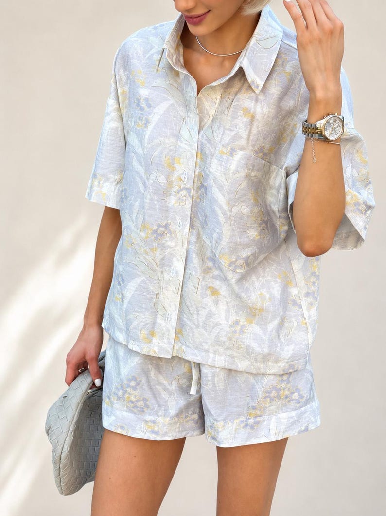 Puede incluir: Conjunto de camisa y pantal&oacute;n corto de lino azul claro con estampado floral amarillo y blanco. La camisa de manga corta tiene botones en la parte delantera y cuello. El pantal&oacute;n corto tiene cintura con cord&oacute;n. Tambi&eacute;n se ve un reloj plateado y un bolso gris.