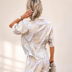 Puede incluir: Conjunto de camisa de manga corta y shorts a juego con estampado floral azul claro. El conjunto presenta un delicado estampado floral en tonos amarillos y blancos. Los pantalones cortos tienen bolsillos. Se sostiene un peque&ntilde;o bolso de mano tejido.