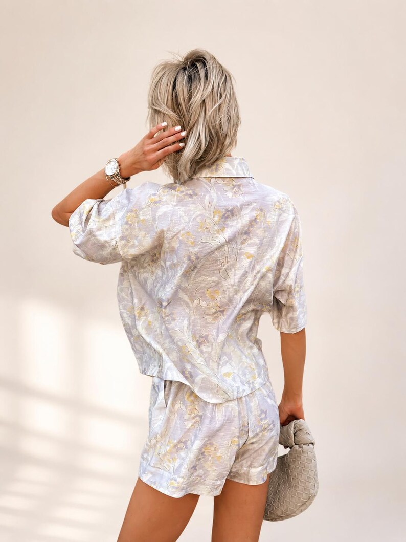 Puede incluir: Conjunto de camisa de manga corta y shorts a juego con estampado floral azul claro. El conjunto presenta un delicado estampado floral en tonos amarillos y blancos. Los pantalones cortos tienen bolsillos. Se sostiene un peque&ntilde;o bolso de mano tejido.