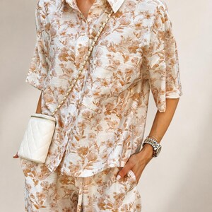 Puede incluir: Conjunto de dos piezas con estampado floral crema y marr&oacute;n. El conjunto incluye una camisa con botones y mangas cortas y pantalones a juego. Un peque&ntilde;o bolso cruzado acolchado blanco con cadena dorada.