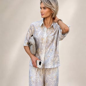 Puede incluir: Un conjunto de dos piezas a juego con una camisa con botones y pantalones de pernera ancha. El conjunto est&aacute; adornado con un estampado floral en tonos azul claro, blanco y amarillo. Un peque&ntilde;o clutch texturizado y una funda blanca para tel&eacute;fono completan el conjunto.