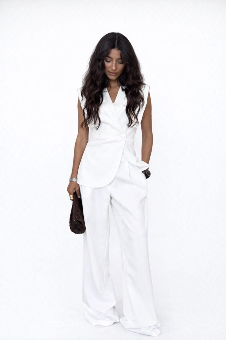 May include: A white sleeveless blazer and wide-leg trousers. The blazer features a double-breasted design with two buttons. The outfit is a monochromatic ensemble, suitable for formal or business wear.