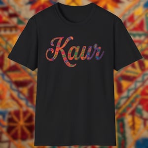 Peut inclure: T-shirt noir avec le nom "Kaur" dans un motif floral coloré. Le mot est écrit en cursive avec des teintes de rouge, orange, jaune, vert, bleu et violet. Le t-shirt est fait d'une matière douce.