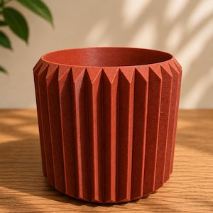 Peut inclure: Un pot de fleurs cylindrique de couleur terre cuite avec un design géométrique à arêtes. Le pot a une large ouverture et est fait d'un matériau texturé. Le design présente des arêtes triangulaires verticales. Convient pour l'intérieur ou l'extérieur.