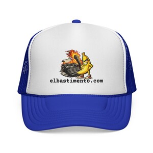 May include: A blue and white trucker hat featuring a cartoon banana with a microphone and a burning typewriter. The text "elbastimento.com" is printed below the graphic. The hat has a blue brim and mesh back.