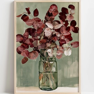May include: A framed wall art print featuring a clear glass jar filled with deep burgundy and reddish-brown eucalyptus branches. The background is a soft, muted sage green with visible brushstroke textures, set within a light wood frame.