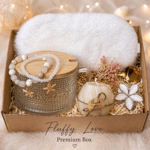 May include: A gift box with a white eye mask, a beaded bracelet with starfish charms, a candle, and a decorative flower. The box is labeled "Fluffy Love Premium Box."