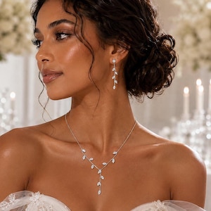 May include: A silver-toned necklace and matching drop earring set featuring a delicate vine motif. The jewelry is adorned with small, clear, marquise-cut stones arranged in a branch-like pattern that follows the neckline and hangs down.