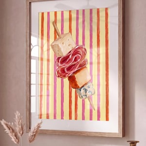 Puede incluir: Impresión en acuarela de una brocheta con queso, salami y otros aperitivos. La brocheta está colocada sobre un fondo de rayas verticales en amarillo, rosa y naranja. La obra de arte está enmarcada en un marco de madera clara.