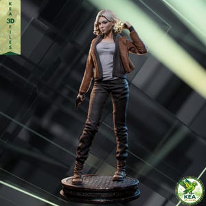 Op de afbeelding: Een gedetailleerd 3D-geprint beeldje van een vrouw die een zaklamp en een pistool vasthoudt. Ze draagt een bruine jas, een grijs shirt en een donkere broek. Het beeldje staat op een rond platform. De tekst "KEA 3D FILES" is inbegrepen.