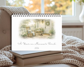 Puede incluir: Un calendario encuadernado en espiral con una ilustración en acuarela de un porche con una mecedora, una mesa y una puerta. El texto "A Year on Memaw's Porch 2026" está impreso. El calendario está sobre una pila de libros.