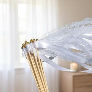 May include: A white wedding wand with a lace veil and white ribbons. The wand features gold accents and is made with wooden dowels. The veil is made of delicate lace.
