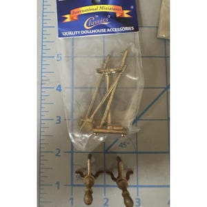Può includere: Un set di accessori per casa delle bambole in metallo color oro, inclusi due supporti a forma di cavalletto e due piccoli terminali decorativi. Gli articoli sono confezionati in un sacchetto di plastica trasparente con l'etichetta International Miniatures by Classics.