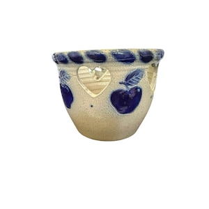 May include: A beige ceramic bowl with a blue rim featuring a braided texture. The bowl is decorated with blue painted apples and cut-out heart shapes around the upper perimeter. The surface has a speckled finish with a darker base tone.