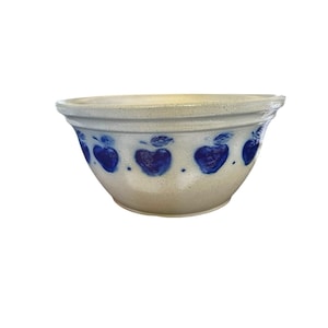 Op de afbeelding: Een beige keramische mengkom met een brede rand en een taps toelopende voet. De buitenkant is voorzien van een herhalend patroon van handgeschilderde blauwe appels met groene blaadjes, gescheiden door kleine blauwe stippen rondom.