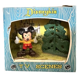 May include: A Disneykin TV Scenes boxed set featuring a small Mickey Mouse figurine with a yellow shirt and red shorts standing next to a green plastic tree. The blue cardboard box displays the text Disneykin and TV SCENES on the front.