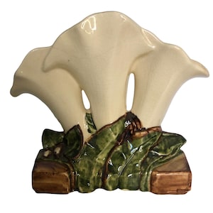 Peut inclure: Un vase en céramique de couleur crème représentant trois fleurs stylisées en forme de trompette émergeant d'une base de feuilles vertes et d'accents rectangulaires bruns. La finition brillante présente un fin motif craquelé.