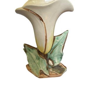 Peut inclure: Un vase en céramique en forme de fleur de lys calla avec une fleur couleur crème et une base jaune. Le vase présente des feuilles vertes avec des détails bruns à la base, créant une apparence naturaliste avec une finition brillante.