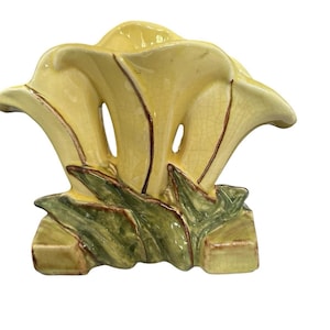 Peut inclure: Un vase en céramique en forme de trois arums jaunes avec une finition émaillée craquelée visible. La base présente des feuilles vertes sculptées avec des détails bruns. L'objet possède une large ouverture évasée et une base rectangulaire.