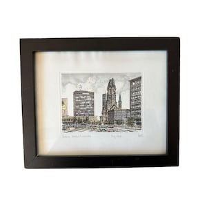 May include: A framed print featuring a detailed ink and watercolor illustration of the Kaiser Wilhelm Memorial Church in Berlin, with the text Berlin, Gedächtniskirche, Rad. and a signature visible at the bottom of the artwork.