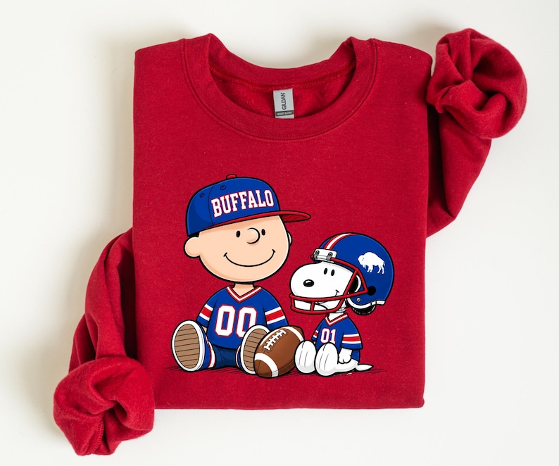 A red sweatshirt with a graphic of two cartoon characters, one wearing a football jersey and the other a baseball cap, sitting next to each other.