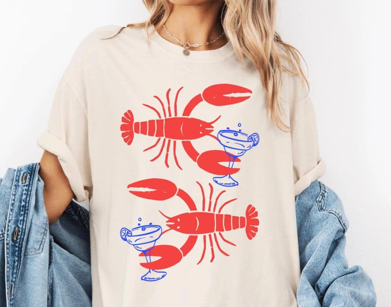 A woman wearing a white t-shirt with a graphic design of two red lobsters holding drinks.