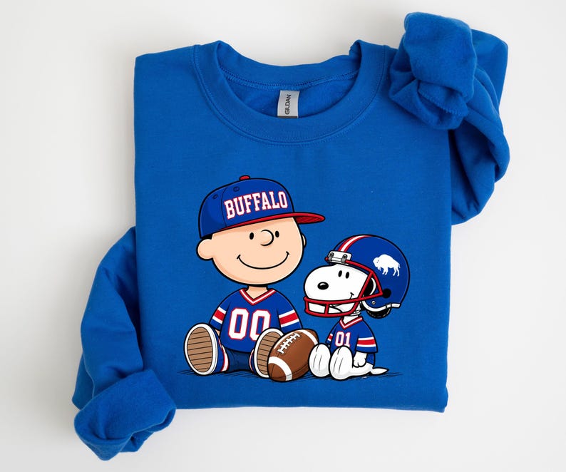 A blue sweatshirt with a graphic of two cartoon characters, one wearing a football jersey and the other a baseball cap, sitting together and smiling.