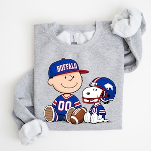 A gray sweatshirt with a graphic design featuring two cartoon characters, a boy and a dog, dressed in football uniforms and holding a football.