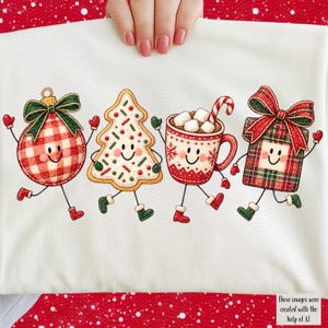 May include: A white t-shirt featuring a graphic print of four anthropomorphic Christmas characters: a red and white checkered ornament, a decorated tree cookie, a mug of hot cocoa with marshmallows, and a plaid gift box, all with smiling faces.