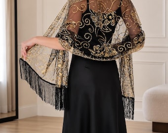 Puede incluir: Un vestido negro sin mangas combinado con un chal negro transparente que presenta intrincados bordados dorados, lentejuelas y largos flecos negros en los bordes. El chal está drapeado sobre los hombros, mostrando un patrón floral y detalles dorados.