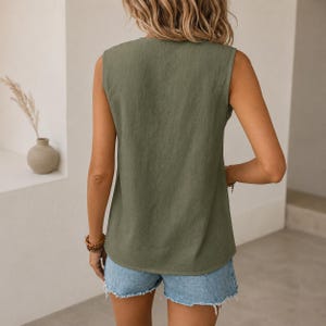 K&ouml;nnte beinhalten: Ein &auml;rmelloses olivgr&uuml;nes Oberteil mit einfachem Rundhalsausschnitt und geradem Saum, kombiniert mit hellblauen Jeansshorts. Das Oberteil hat eine einfarbige Textur und eine lockere Passform, was f&uuml;r ein klares und schlichtes Erscheinungsbild sorgt.