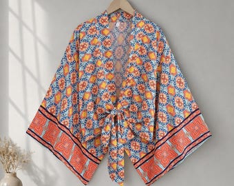 Puede incluir: Un cárdigan ligero estilo kimono con un patrón geométrico vibrante en tonos naranja, amarillo y azul. La prenda tiene mangas anchas y sueltas, frente abierto y un cierre de lazo en la cintura con un borde decorativo ancho en el bajo.