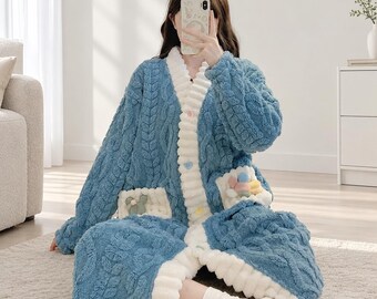 Puede incluir: Un cárdigan azul de manga larga hecho de material polar texturizado y difuso con un patrón de cable. Presenta un borde acanalado blanco grueso a lo largo de la abertura frontal, botones coloridos en forma de corazón y dos bolsillos delanteros con pequeños apliques decorativos.
