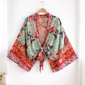 May include: A mint green kimono-style top with a floral pattern in red, pink, and navy blue. The top has wide sleeves and a tie closure at the waist. The edges are trimmed with a red and orange floral border.