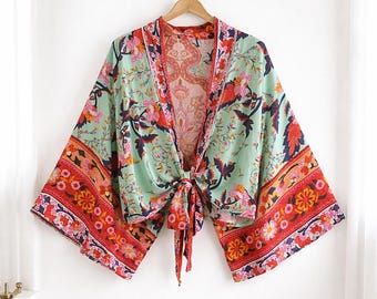 Könnte beinhalten: Ein mintgrünes Kimono-Top mit einem floralen Muster in Rot, Rosa und Marineblau. Das Oberteil hat weite Ärmel und einen Bindverschluss in der Taille. Die Ränder sind mit einem rot-orangen Blumenmuster verziert.