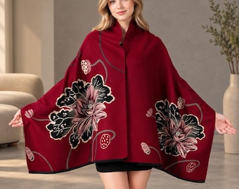 Puede incluir: Un chal de color rojo intenso con un estampado floral grande y detallado de flores de loto rosas y negras con tallos. La prenda tiene una base de color rojo oscuro sólido y un borde negro en los extremos, ofreciendo una amplia cobertura.