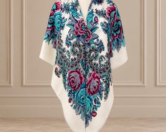 Puede incluir: Un chal blanco con un vibrante estampado floral de grandes rosas magenta y turquesas, acentuado por intrincados remolinos y motivos de follaje en azul oscuro y verde azulado, acabado con un borde delicadamente deshilachado.