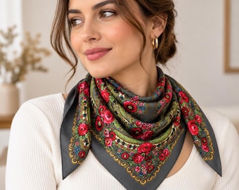 Puede incluir: Un pañuelo cuadrado con fondo gris oscuro y un vibrante estampado floral de rosas rojas, hojas verdes y pequeños detalles en azul y amarillo. El pañuelo está doblado en forma de triángulo y anudado al cuello, mostrando un borde detallado.