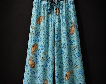 Puede incluir: Pantalones de pierna ancha en tela azul claro con un patrón repetitivo de flores azul oscuro y formas de cachemira marrón dorado. La cintura es elástica con un lazo a juego y un borde floral oscuro, con un dobladillo floral más grande.