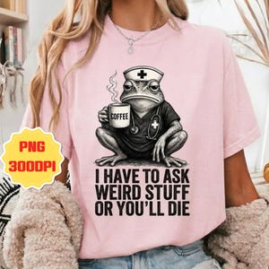 May include: A light pink t-shirt featuring a graphic of a frog dressed as a nurse, wearing a cap with a cross, holding a coffee mug, and wearing a stethoscope. Below the frog, the text reads: I HAVE TO ASK WEIRD STUFF OR YOU'LL DIE.