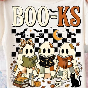 Peut inclure: Un t-shirt crème avec une impression graphique portant le texte "BOO=KS". Le motif représente trois fantômes lisant des livres, entourés d'un damier, de chauves-souris, d'un croissant de lune, d'une bougie, de citrouilles, d'un mug crâne et d'un chat noir.