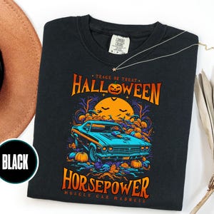 May include: A black t-shirt featuring a graphic print of a blue muscle car surrounded by orange pumpkins and a large yellow moon. The text reads "TRACK OR TREAT HALLOWEEN HORSEPOWER MUSCLE CAR MADNESS" in orange and yellow lettering.